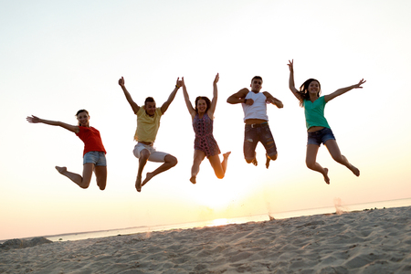 friendship, summer vacation, holidays, party and people concept - group of smiling friends dancing and jumping on beachの写真素材