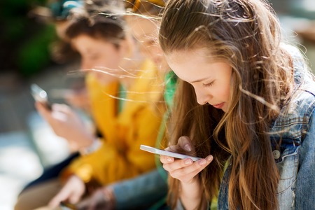 technology, internet addiction and people concept - happy teenage friends with smartphones outdoors