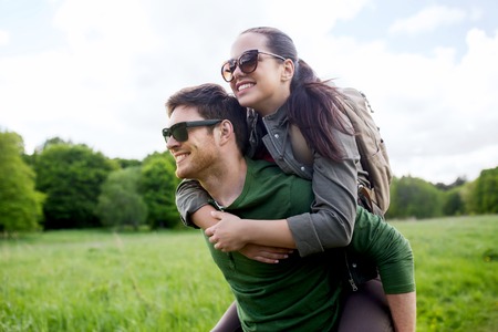 travel, hiking, backpacking, tourism and people concept - happy couple in sunglasses with backpacks having fun and walking along country road outdoorsの写真素材