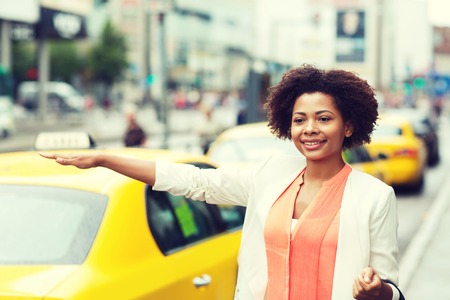 business trip, transportation and people concept - young smiling african american woman catching taxi at city streetの写真素材