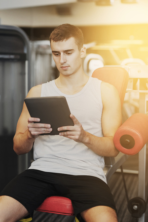 sport, bodybuilding, lifestyle, technology and people concept - young man with tablet pc computer in gymの写真素材