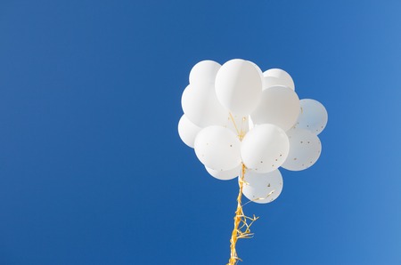 holidays, birthday, party and decoration concept - close up of inflated white helium balloons in blue skyの写真素材