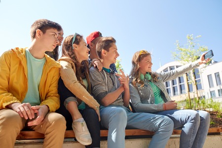 education, high school, technology and people concept - group of happy teenage students or friends taking selfie by smartphoneの写真素材