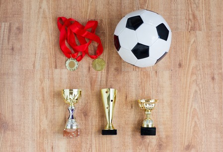 sport, achievement, championship, competition and success concept - football or soccer ball with golden medals and cups over wooden backgroundの写真素材