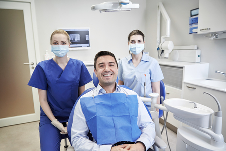 people, medicine, stomatology and health care concept - happy female dentists with man patient at dental clinic officeの写真素材