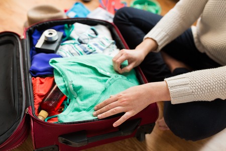 summer vacation, travel, tourism and objects concept - close up of woman packing travel bag for...