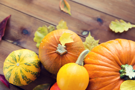 harvest, season, advertisement and autumn concept - close up of pumpkins and leaves on wooden table at homeの写真素材