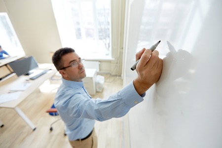 education, school, teaching and people concept - teacher writing something on white board in classroomの写真素材