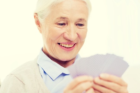 age, game, gamble, poker and people concept - happy smiling senior woman playing cards at homeの写真素材