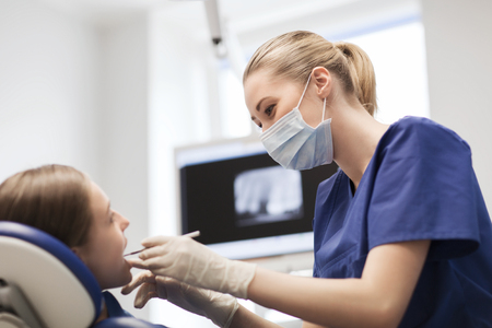 people, medicine, stomatology and health care concept - happy female dentist with mirror or dental probe checking patient girl teeth up at dental clinic officeの写真素材