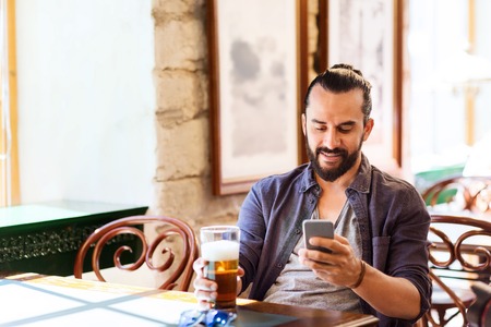 people and technology concept - man with smartphone drinking beer and reading message at bar or pubの写真素材