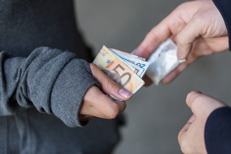drug trafficking, crime, addiction and sale concept - close up of addict with money buying dose from dealer on streetの写真素材
