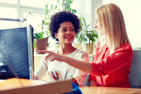 business, education, startup and people concept - happy women or students with computer in officeの写真素材