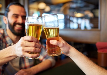 people, men, leisure, friendship and celebration concept - happy male friends drinking beer and clinking glasses at bar or pubの写真素材