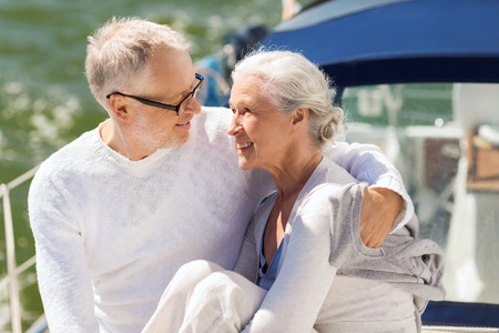 sailing, age, tourism, travel and people concept - happy senior couple hugging on sail boat or yacht deck floating in seaの写真素材