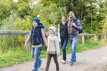 adventure, travel, tourism, hike and people concept - happy family walking with backpacks in woods