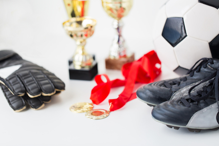 sport, achievement, championship and success concept - close up of soccer ball, football boots and goalkeeper gloves with golden medals and cupsの写真素材