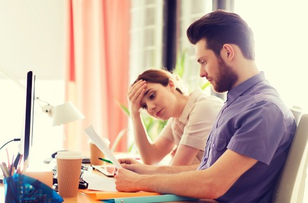 business, startup and people concept - creative team of man and woman with computer and files solving problem in officeの写真素材