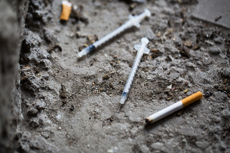 smoking, substance abuse, addiction and drug use concept - close up of syringe and smoked cigarette on groundの写真素材