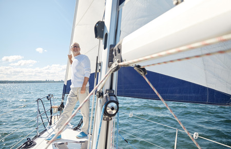 sailing, age, tourism, travel and people concept - happy senior man on sail boat or yacht floating in seaの写真素材