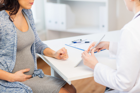 pregnancy, gynecology, medicine, health care and people concept - close up of gynecologist doctor showing tablet pc computer to pregnant woman at hospitalの写真素材