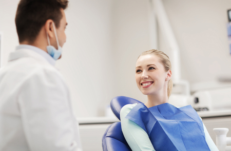 people, medicine, stomatology and health care concept - happy male dentist with woman patient talking at dental clinic officeの写真素材