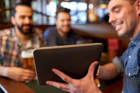 people, men, leisure, friendship and technology concept - happy male friends with tablet pc computer drinking beer at bar or pubの写真素材