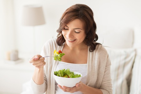 healthy eating, dieting and people concept - smiling young woman eating vegetable salad at homeの写真素材