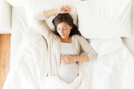 pregnancy, rest, people and expectation concept - happy pregnant woman sleeping in bed at homeの写真素材