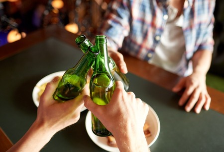 people, men, leisure, friendship and celebration concept - close up of male friends drinking beer and clinking bottles at bar or pubの写真素材