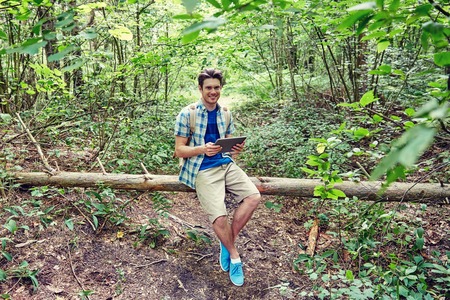 adventure, travel, tourism, hike and people concept - happy young man with backpack and tablet pc...