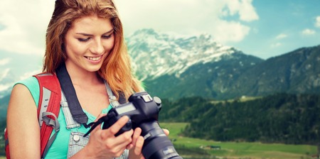 adventure, travel, tourism, hike and people concept - happy young woman with backpack and camera photographing over alps mountains backgroundの写真素材