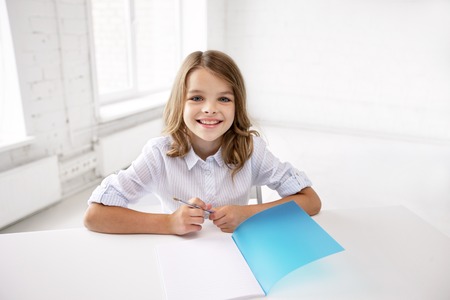 education, elementary school, learning and people concept - happy smiling girl with notebook and penの写真素材