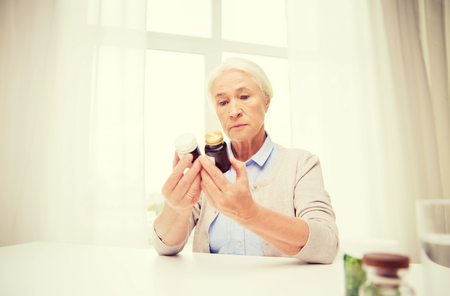age, medicine, health care and people concept - senior woman looking at jars with medicine at home or hospital officeの写真素材