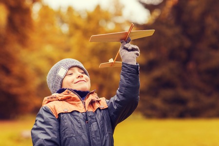 autumn, childhood, dream, leisure and people concept - happy little boy playing with wooden toy plane outdoorsの写真素材