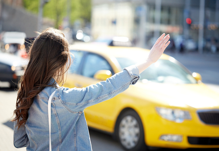gesture, transportation, travel, tourism and people concept - young woman or teenage girl catching taxi on city street or hitch-hikingの写真素材