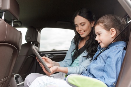 family, transport, road trip, travel and people concept - happy woman and little daughter with tablet pc computer driving in carの写真素材