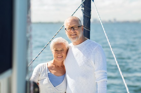 sailing, age, tourism, travel and people concept - happy senior couple hugging on sail boat or yacht deck floating in seaの写真素材