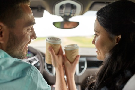 leisure, road trip, travel, family and people concept - happy man and woman driving in car with coffeeの写真素材