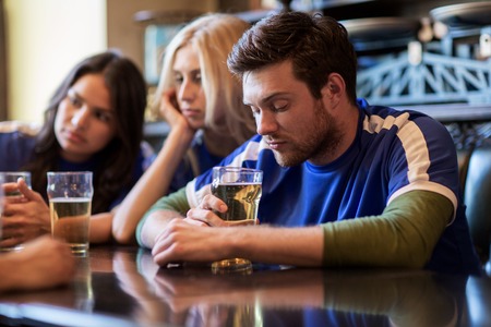 people, leisure, soccer and sport concept - unhappy football fans or friends with beer at bar or pubの写真素材