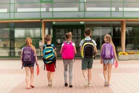 primary education, friendship, childhood and people concept - group of happy elementary school students with backpacks walking outdoors from backの写真素材