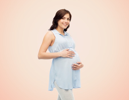 pregnancy, motherhood, people and expectation concept - happy pregnant woman touching her big belly...