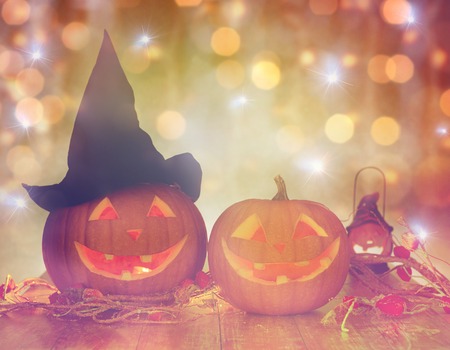 holidays, halloween and decoration concept - close up of carved pumpkins with smiley faces and witch hat on table over lightsの写真素材