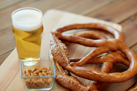 food, baking, cooking and pastry concept - close up of beer in glass, pretzels and peanuts on wooden tableの写真素材