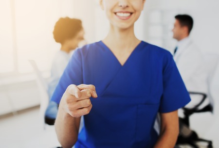 gesture, people and medicine concept - close up of happy female doctor or nurse pointing finger on you over group of medics meeting at hospitalの写真素材