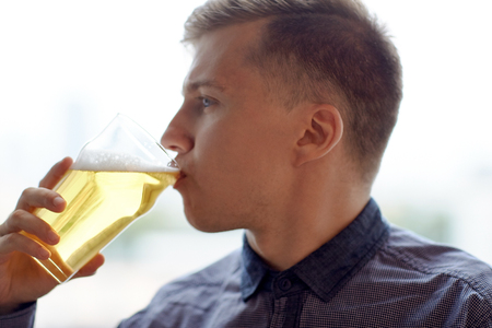 people, drinks, alcohol and leisure concept - close up of young man drinking beer from glassの写真素材