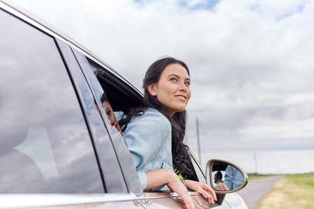summer vacation, holidays, travel, road trip and people concept - happy young woman driving in carの写真素材