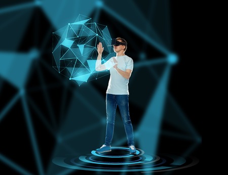 3d technology, augmented reality, gaming, cyberspace and people concept - happy young man with virtual reality headset or 3d glasses playing game and touching low poly shape hologramの写真素材
