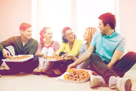 food, leisure and happiness concept - five smiling teenagers eating pizza at homeの写真素材