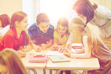 education, elementary school, learning and people concept - teacher helping school kids writing test in classroomの写真素材